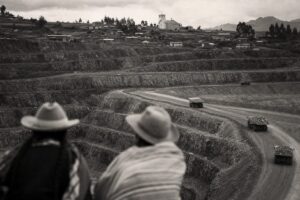 Open-pit mine on a Latin American mountainside with haul trucks, a farming village and church on the ridge (AI-generated image)