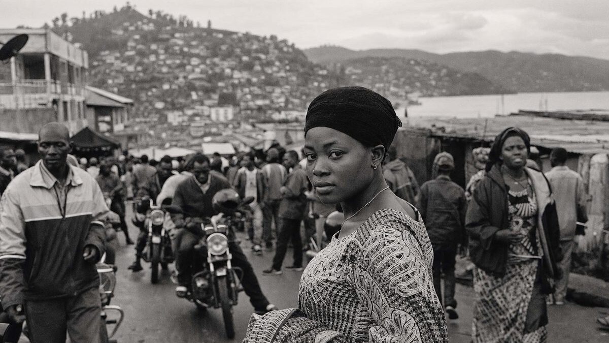 Market street in Bukavu with motorbike taxis and dense buildings climbing the hillside above Lake Kivu (AI-generated image)