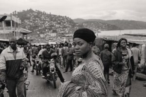 Market street in Bukavu with motorbike taxis and dense buildings climbing the hillside above Lake Kivu (AI-generated image)