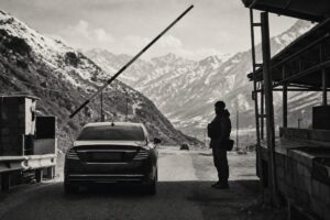Mountain road checkpoint in the South Caucasus with a raised barrier, a waiting sedan and a lone soldier (AI-generated image)