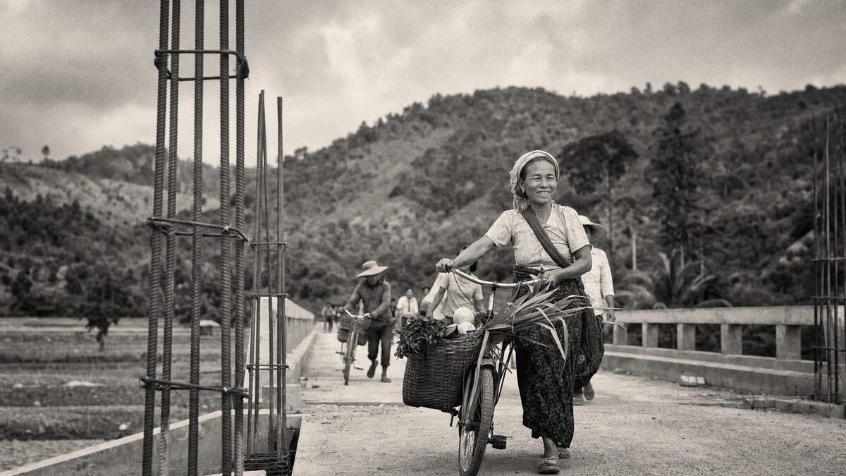 Villagers with bicycles and produce crossing a newly built rural footbridge, green hills behind (AI-generated image)