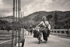 Villagers with bicycles and produce crossing a newly built rural footbridge, green hills behind (AI-generated image)