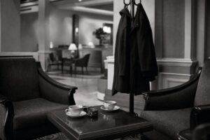 Quiet hotel lounge used for back-channel talks, two coats on a rack and two coffee cups between armchairs (AI-generated image)
