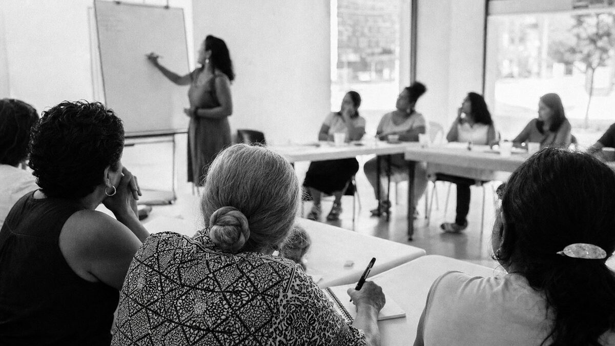 Women's civil-society workshop in a community centre, a facilitator at a whiteboard, participants taking notes (AI-generated image)