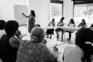 Women's civil-society workshop in a community centre, a facilitator at a whiteboard, participants taking notes (AI-generated image)
