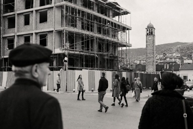 Town square in Kosovo with a half-built administration building under scaffolding and an Ottoman clock tower (AI-generated image)
