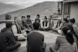 Local peace committee seated on mats in a Nepali hill village courtyard, terraced foothills behind (AI-generated image)