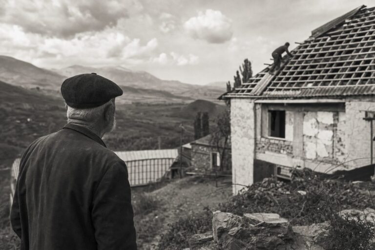 Hillside village in Georgia, a house roof under repair, an elderly man looking across the valley (AI-generated image)
