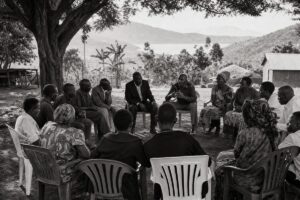 Community reconciliation meeting in a circle of plastic chairs under an acacia tree in the Great Lakes region (AI-generated image)