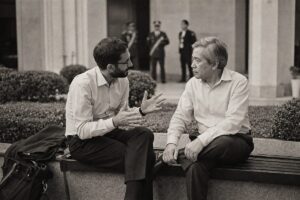 Two negotiators from opposing sides talking quietly on a courtyard bench away from the conference hall (AI-generated image)
