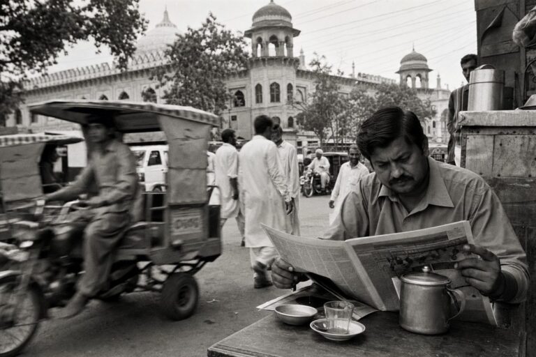 Busy Lahore street with rickshaws and pedestrians in front of a government building (AI-generated image)